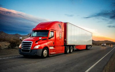 Brightly Red Colored Semi-Truck Speeding on a Two-Lane Highway with Cars in Background Under a Stunning Sunset in the American Southwest