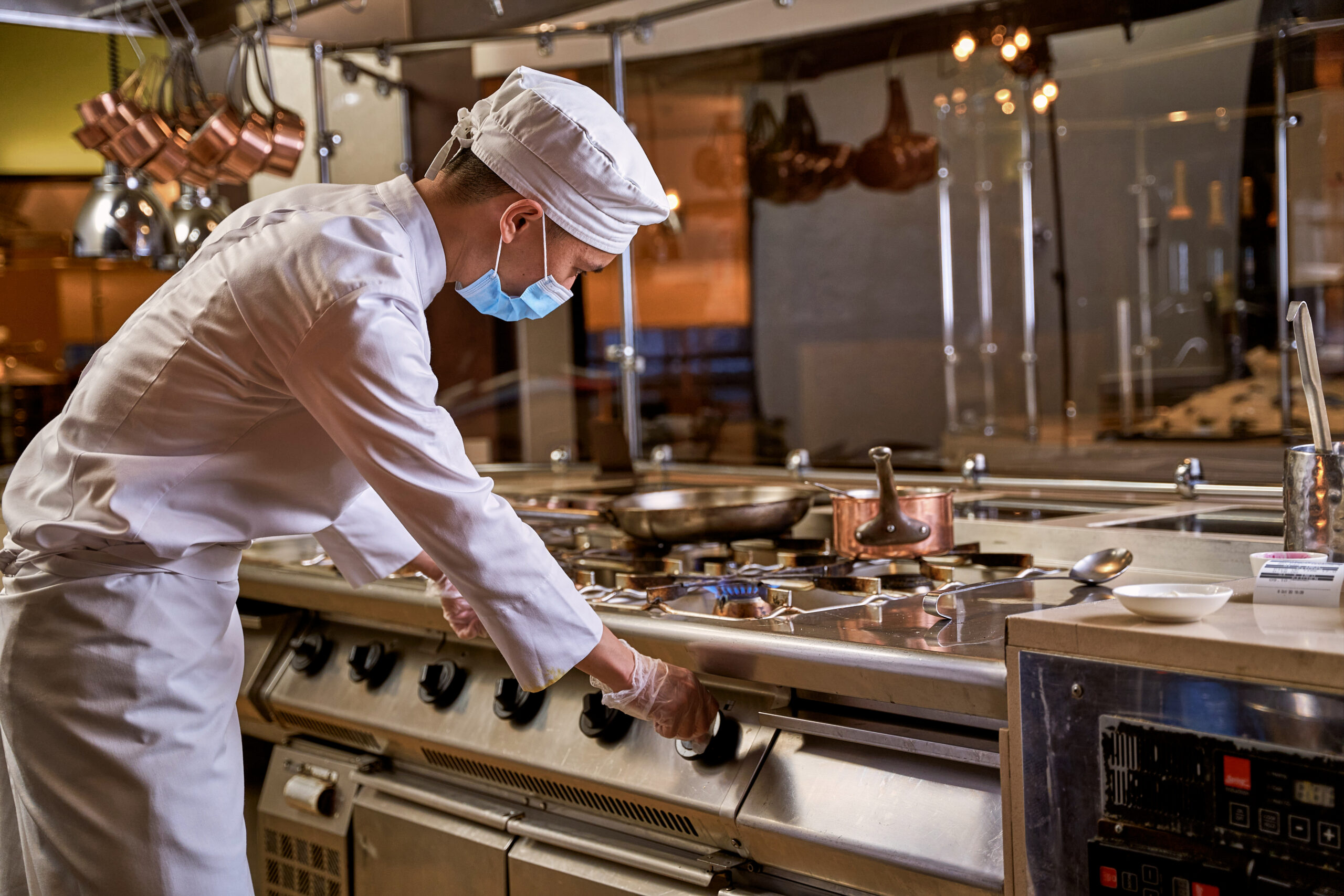Young kitchen worker twisting cooker knob on the right and turning on fire on one burner